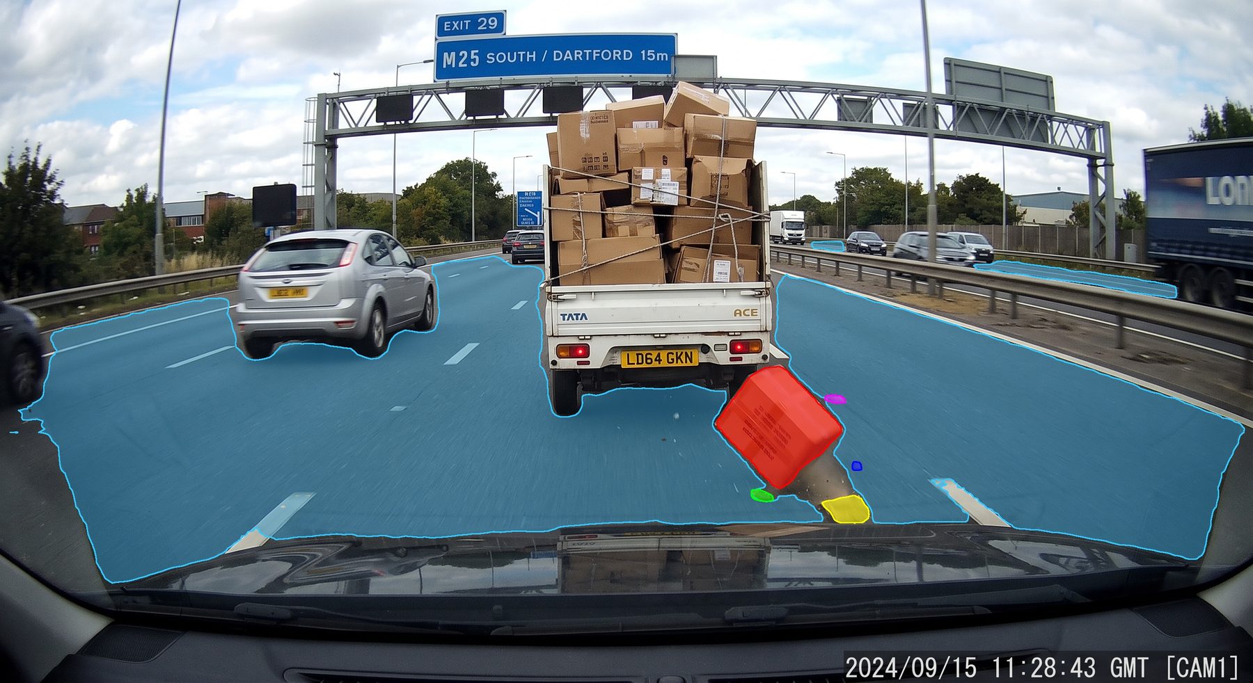 Motorway dashcam frame with the drivable road segmented in blue and a fallen box flagged in red